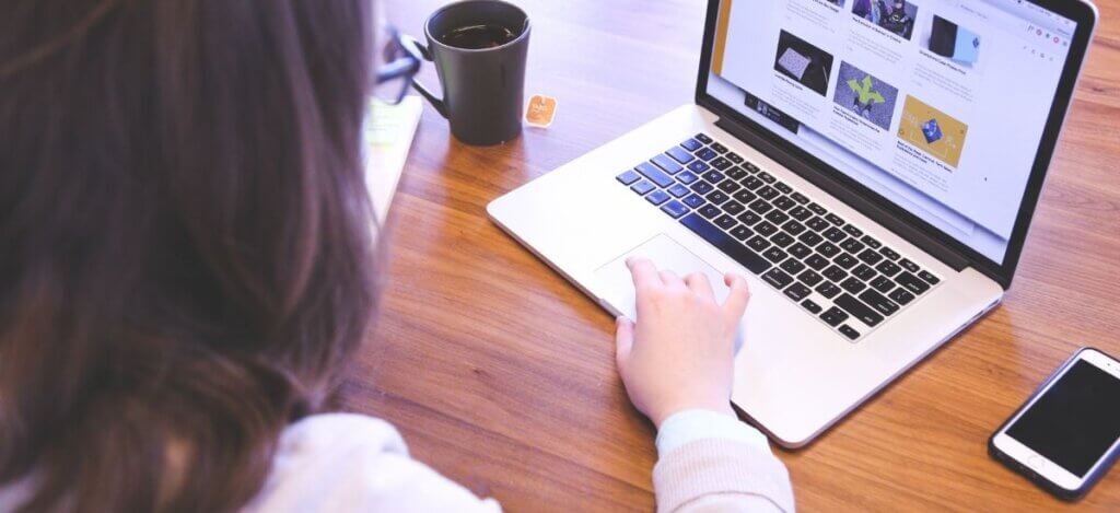 Person bedient eine Laptop, neben welchem eine Tasse Tee steht.